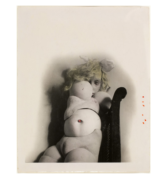 A photograph of a doll like figure with a nude body and segmented stomach, pelvis, and breasts. The doll appears to be lying down or sitting, perhaps on a chair, and has blonde wavy hair.