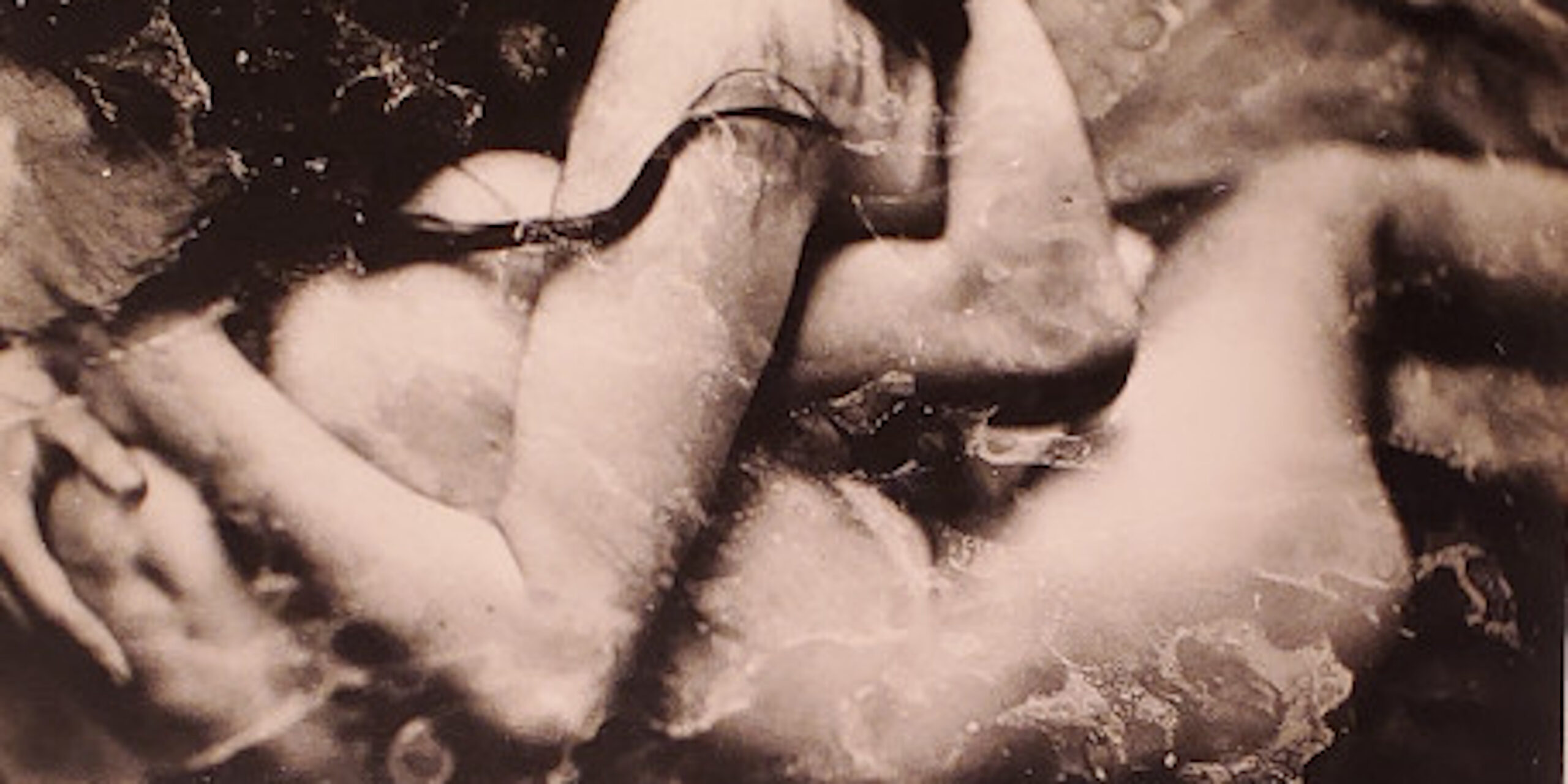 An image showing two nude figures embracing. Their faces are hidden, with the woman's hair covering the face of the other figure. The image has an overall marbled effect.