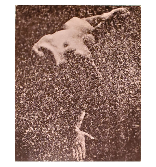 A photograph with an overall speckled effect showing a nude figure. The figure appears to the stretched out with their hands together and their back up, with their knees bent.