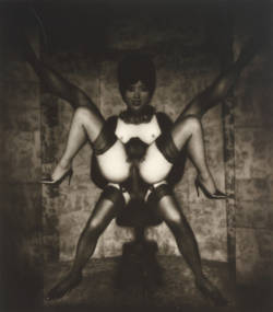This is a work of art. Please note that as it is impossible to know the intent of the artist, the work is subject to interpretation. Each visitor may view and choose to understand the work differently. All effort has been made to provide a purely visual description. A black and white collage photo, that shows a person leaning or sitting on a stool, wearing sheer thigh high stockings. Another person appears to be sitting on top of the first person with their legs spread and a phallic object inserted. The person's chest is bare and they have a beehive hairstyle. Another set of legs appears spread from the top of the person's shoulders.